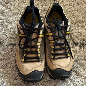 Beige and black Merrell sneakers with yellow details, ideal for hiking.